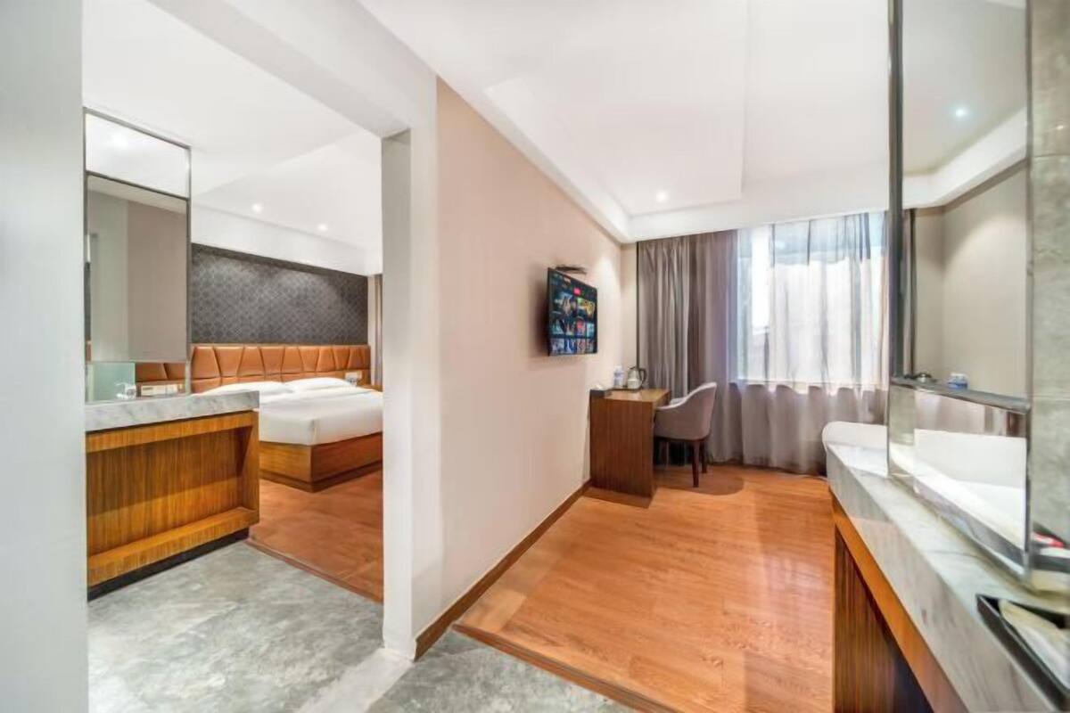 Ein modernes Hotelzimmer mit Holzboden, einem großen Bett, einem separaten Badezimmer mit Waschtisch und einem an der Wand montierten Fernseher.
