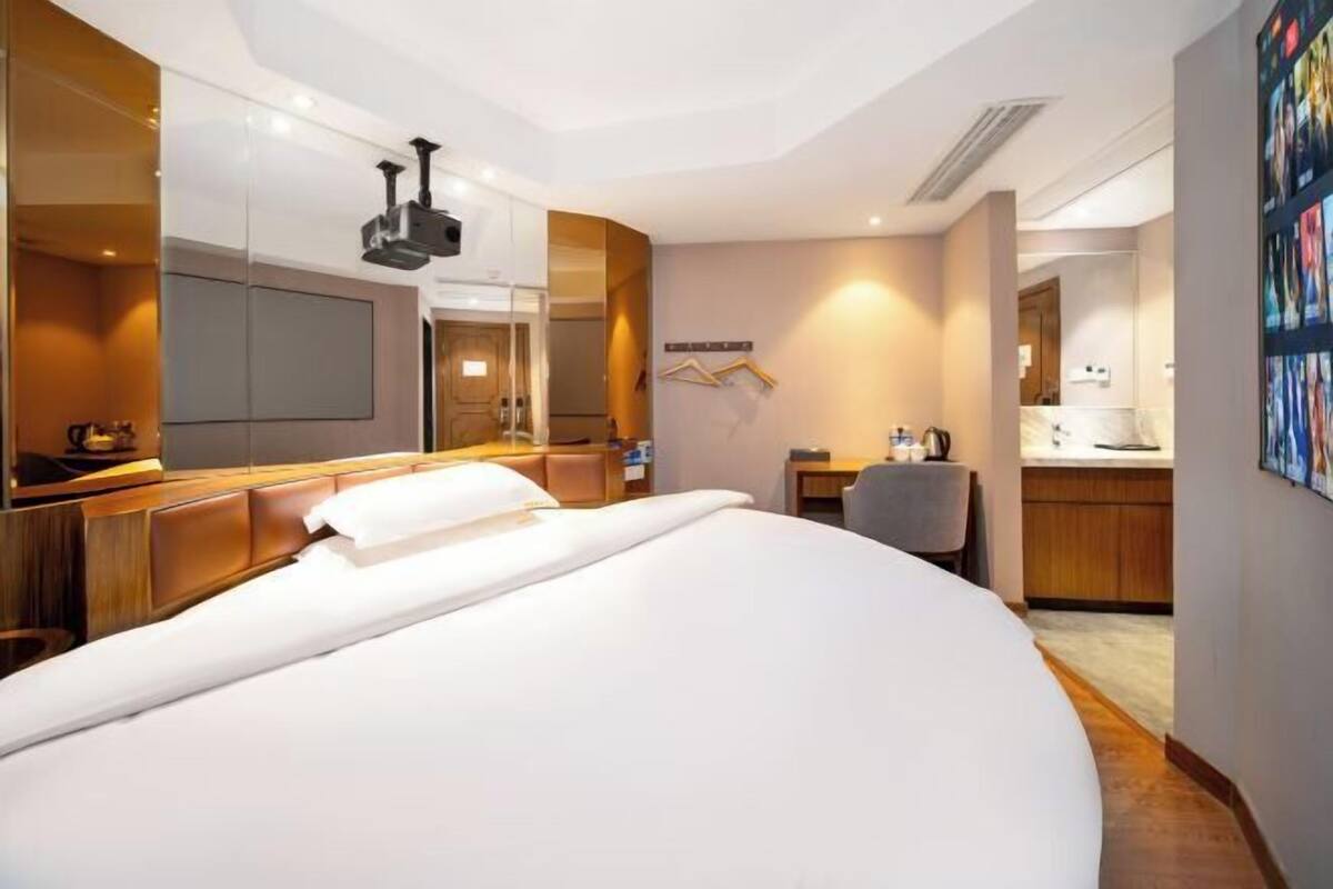 Ein Hotelzimmer mit einem großen Bett, einem Schreibtisch, einem Sessel, einem Spiegel und einem Fernseher.