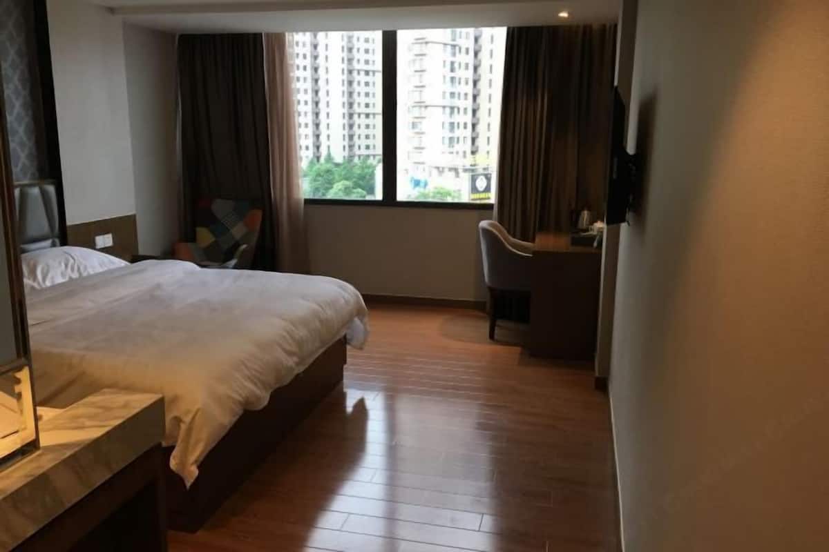 A hotel room with a large bed, a desk, and a view of tall buildings through the window.