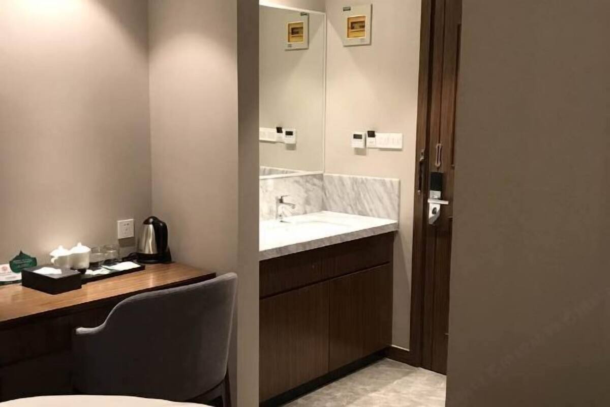 Ein Badezimmer im Hotel mit einem Marmorwaschbecken, Holzschränken, einem Spiegel und einem Schreibtisch mit Stuhl und Pflegeartikeln.