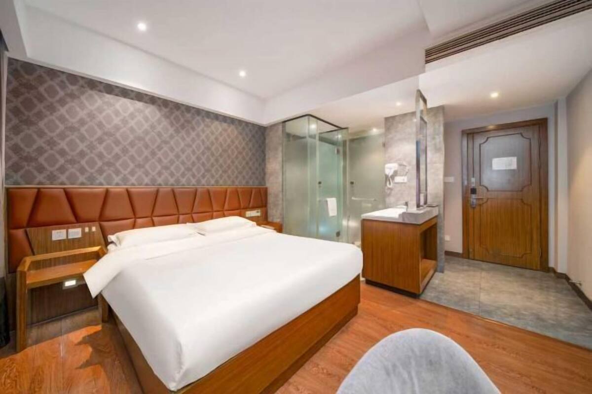 Ein Hotelzimmer mit Bett, Nachttisch, einer Duschkabine, einer Holztür und einem kleinen Schreibtisch mit Stuhl.