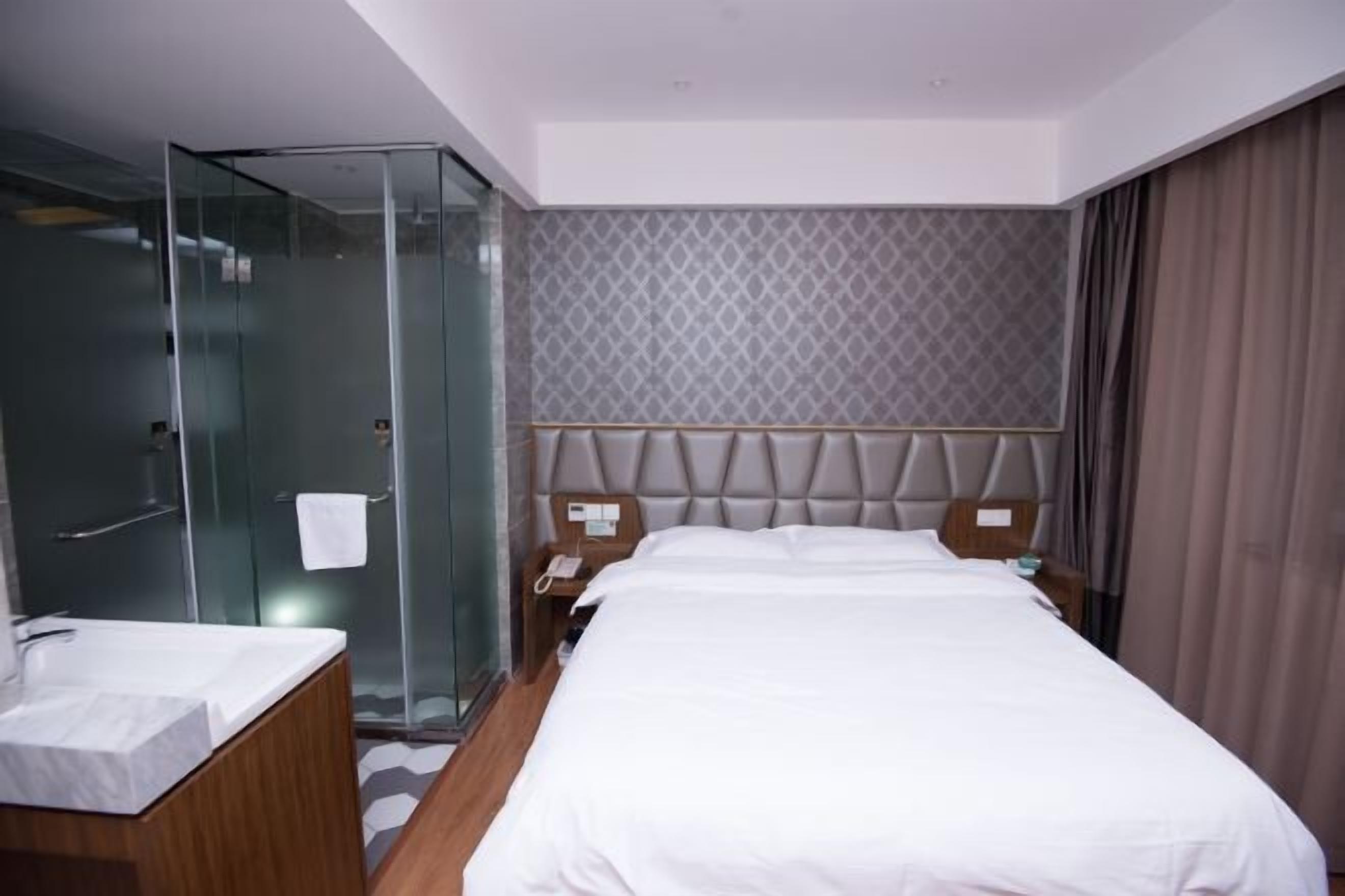 Ein Hotelzimmer mit einem großen Bett, einer Duschkabine aus Glas und einem Holzanrichte mit Waschbecken.