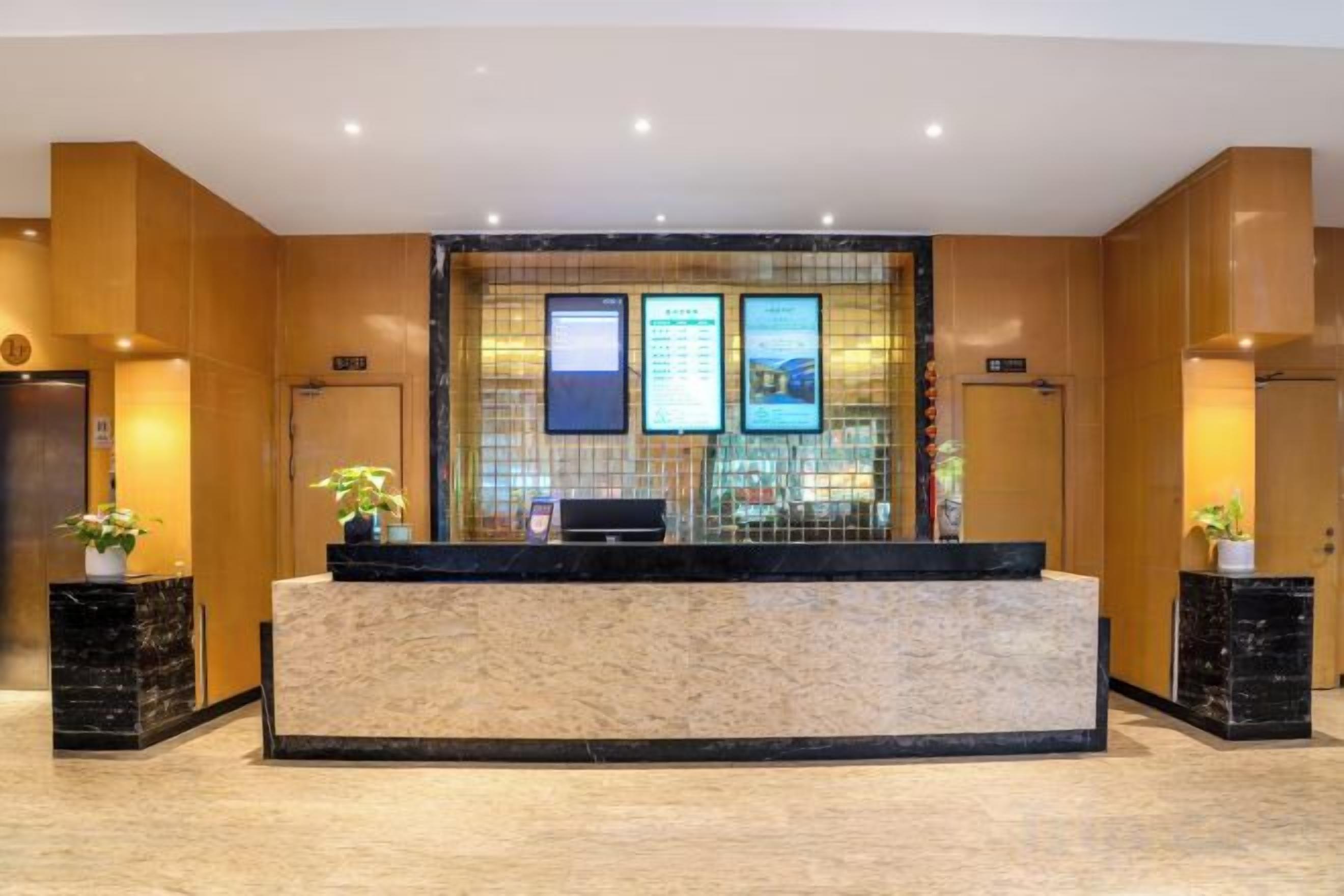 A reception area with a marble counter, two potted plants, and a wall-mounted TV screen.