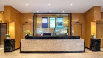 A reception area with a marble counter, two potted plants, and a wall-mounted TV screen.