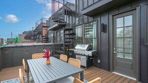 Terrassa al terrat amb taula, cadires, una barbacoa i una escala espiraltra.