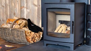A wood-burning stove with a basket of firewood and a loaf of bread nearby. - The Safari Lodge at Rusty Lane Farm (Seend)
