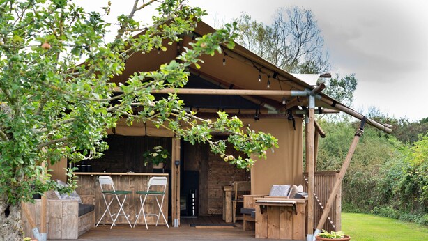 A wooden cabin with a deck, outdoor seating, and a fireplace. - The Safari Lodge at Rusty Lane Farm (Seend)