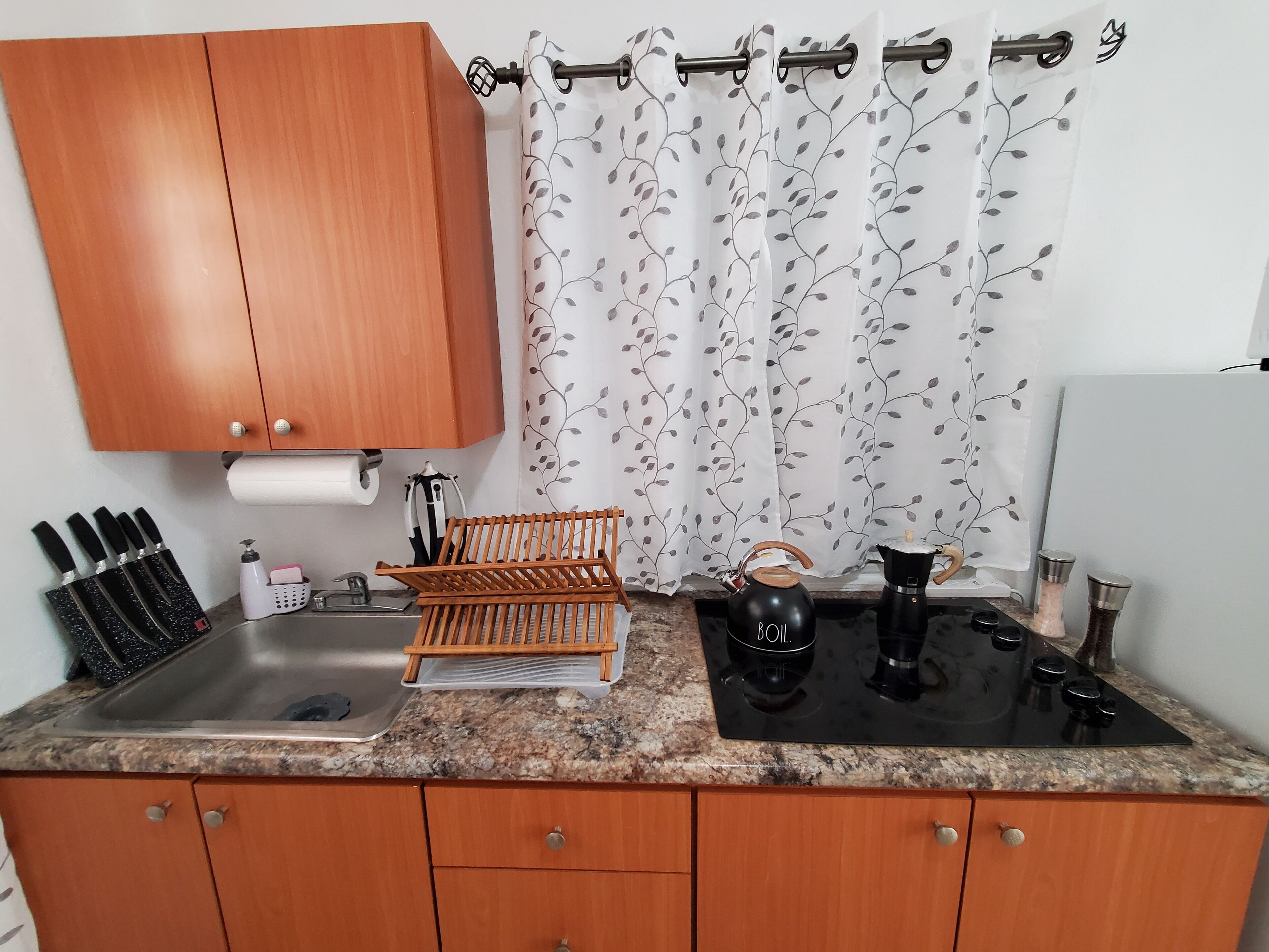 Een keuken met houten kasten, een spoelbak, een fornuis en een waterkoker.