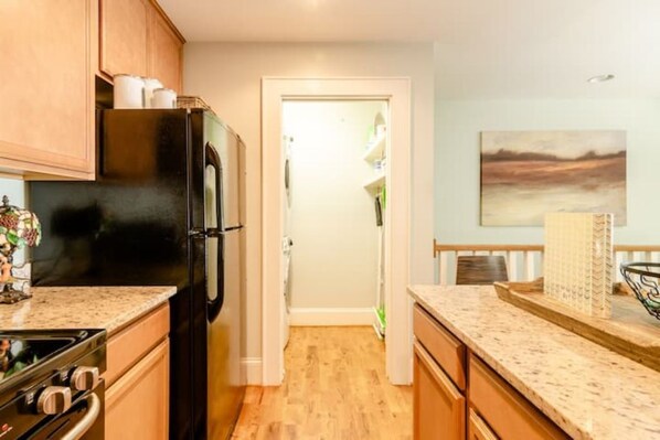 A kitchen with wooden cabinets, a black refrigerator, a granite countertop, and a painting on the wall.