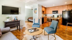 Una sala de estar moderna con una televisión de pantalla plana, un sofá, una mesa de centro y una zona de cocina con armarios de madera y electrodomésticos.