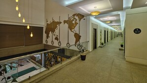 A hotel lobby with a world map mural, a staircase, and a long corridor with doors. - Pride Biznotel Manjusar (Savli)