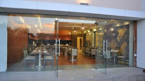 A restaurant with a modern interior, featuring glass partitions and a variety of seating arrangements. - Pride Biznotel Manjusar (Savli)