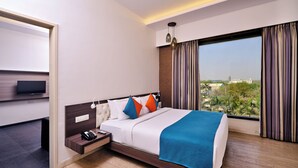 A modern hotel room with a large bed, a desk with a flat-screen TV, and a view of the cityscape. - Pride Biznotel Manjusar (Savli)