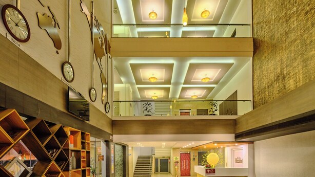 A spacious lobby with a high ceiling, multiple clocks, a reception desk, and a staircase leading to an upper level. - Pride Biznotel Manjusar (Savli)