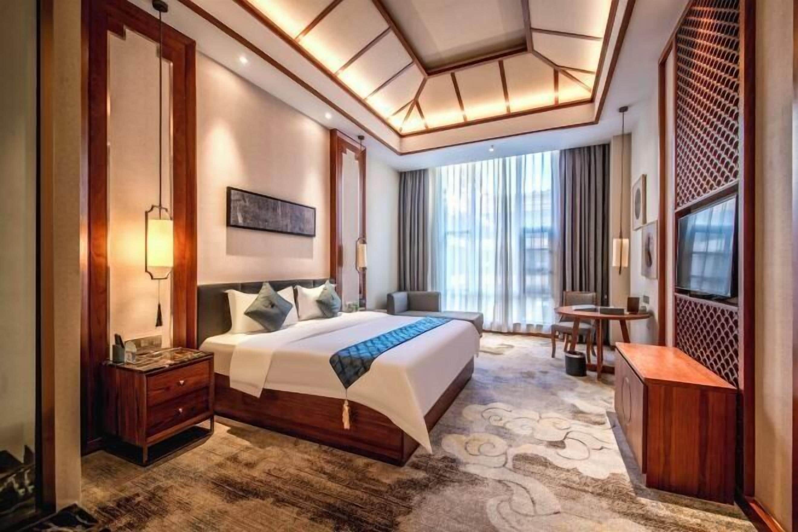 A hotel room with a large bed, a desk, a TV, and a view of the outdoors.