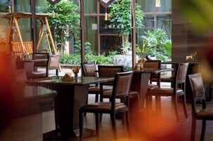 An indoor dining area with tables and chairs, large windows, and potted plants.