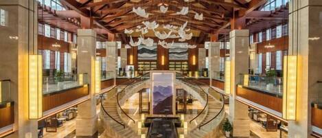 A spacious lobby with a central staircase, high ceilings with wooden beams, and a large mural on the back wall.