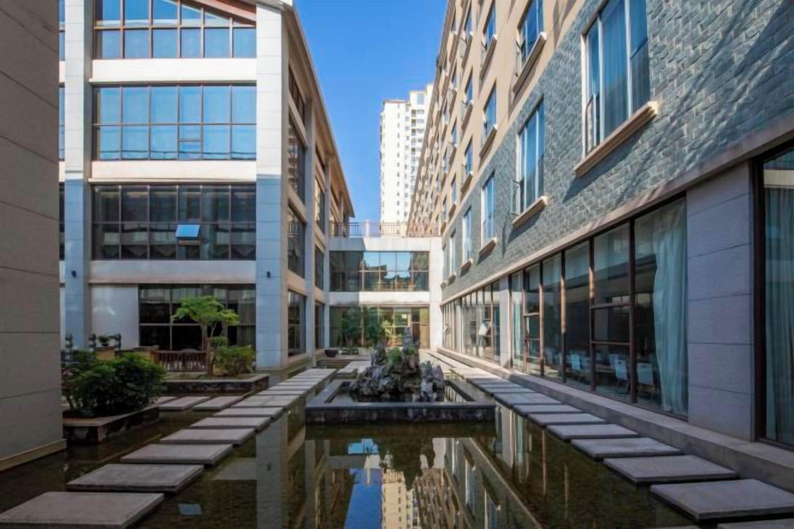 Un patio con una fuente de agua reflectante, edificios modernos y cielo despejado.