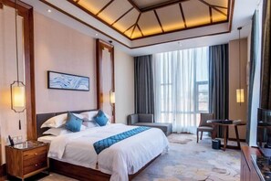 Habitación de hotel con una cama grande, un escritorio, una silla, un televisor y una ventana con cortinas.