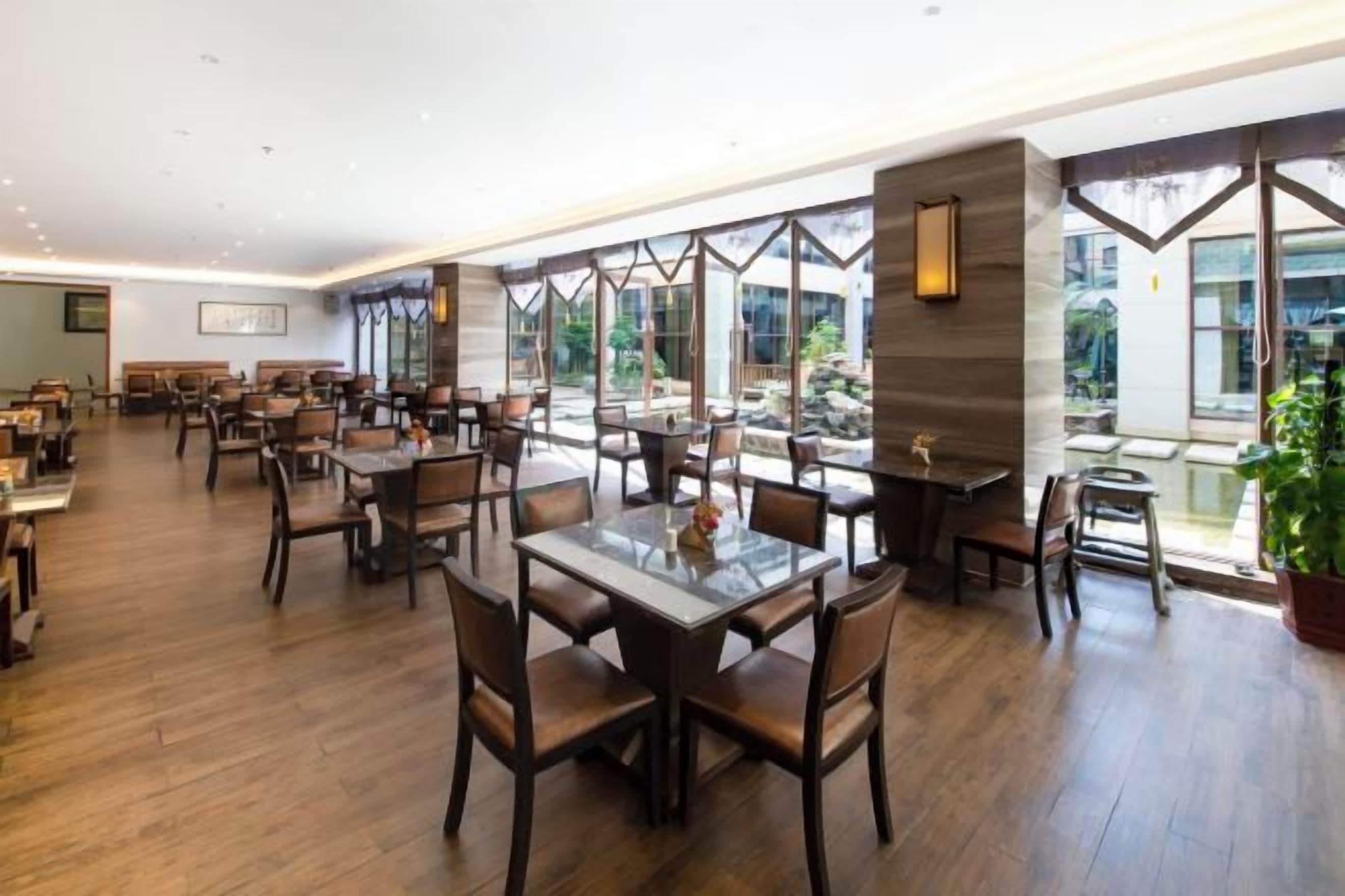 A spacious restaurant with multiple dining tables and chairs, large windows offering views of the outdoors, and a modern interior design.
