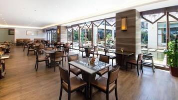 A spacious restaurant with multiple dining tables and chairs, large windows offering views of the outdoors, and a modern interior design.