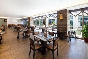 A spacious restaurant with multiple dining tables and chairs, large windows offering views of the outdoors, and a modern interior design. - Yuanmou Grand Hotel (Yuanmou)