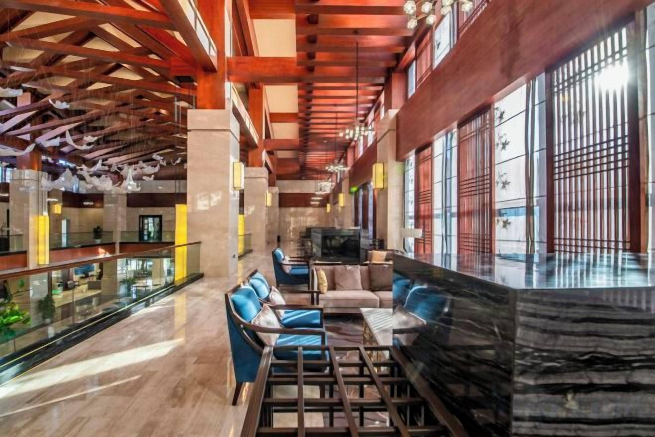 A spacious lobby with a high ceiling, a seating area with blue chairs, and a large window with bars.