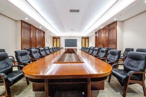 Un salón de conferencias con una larga mesa y sillas, una pantalla de proyector y paneles de madera en las paredes.