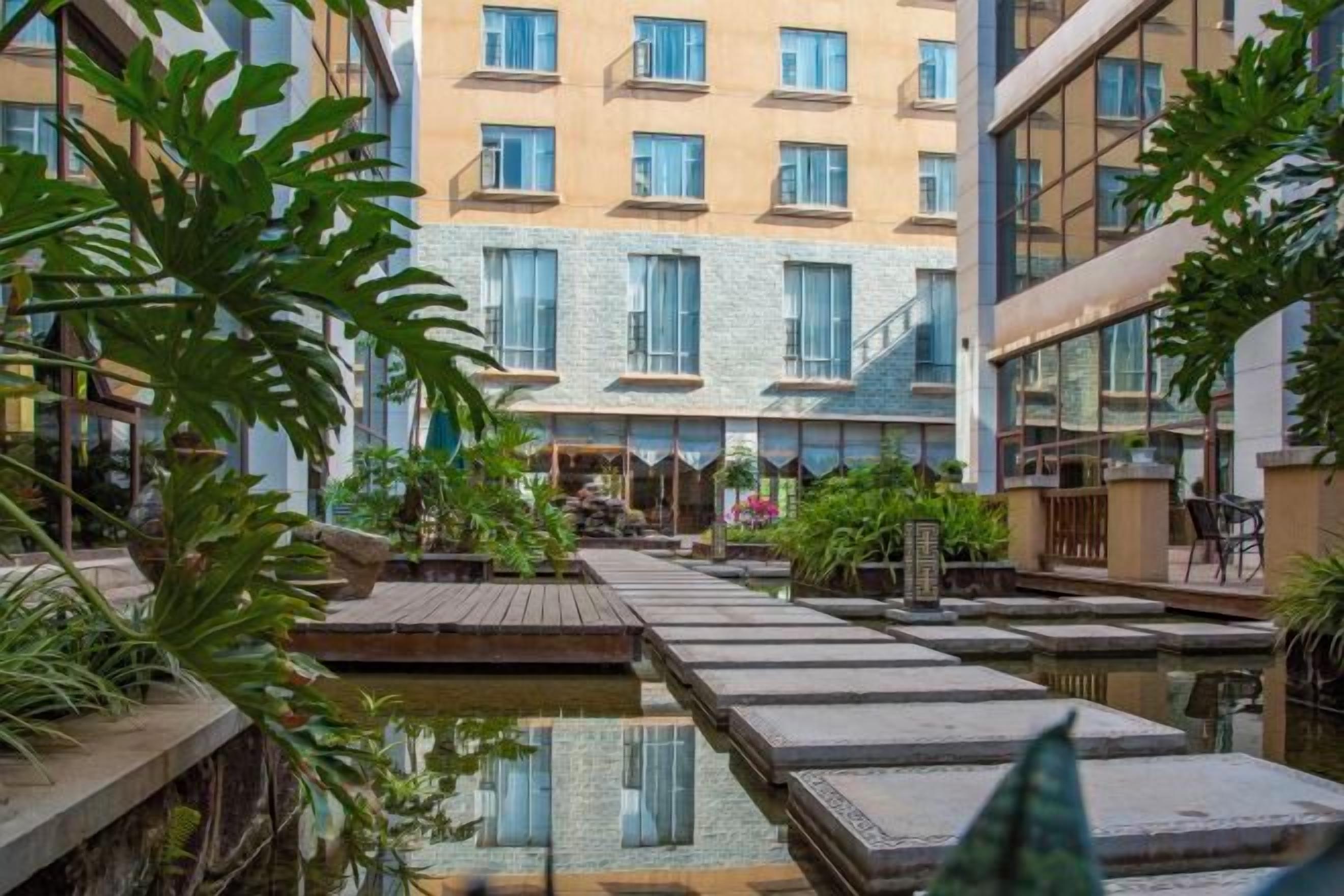 A hotel courtyard with a central water feature, wooden walkways, and surrounding greenery.