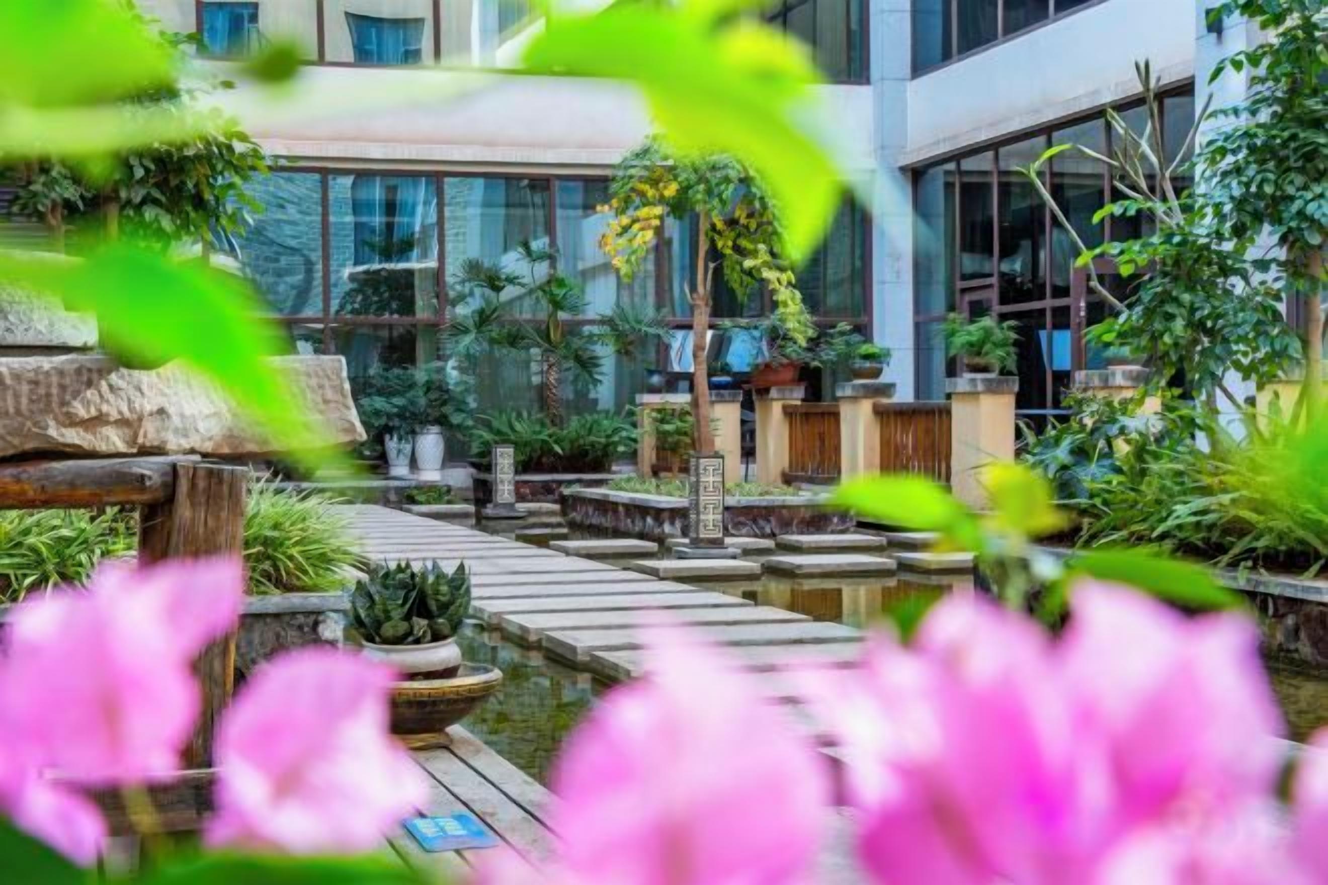 Un patio con una fuente de agua, plantas en macetas y un puente de madera.