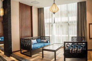 A modern living room with a sofa, a glass coffee table, and a chair with geometric patterns. - Yuanmou Grand Hotel (Yuanmou)