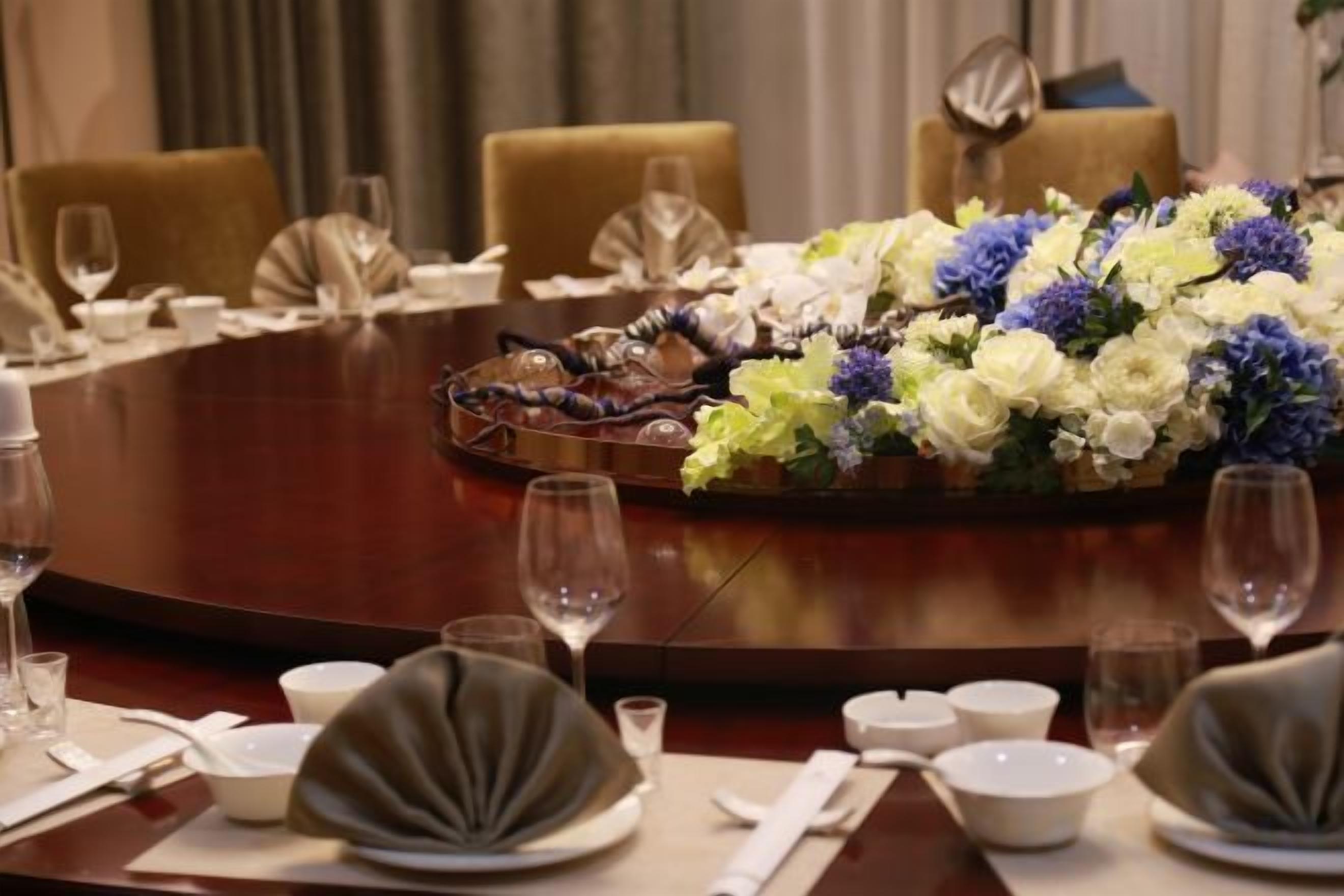 A round dining table set for a formal meal with a floral centerpiece, fine china, and wine glasses.