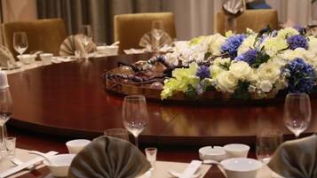A round dining table set for a formal meal with a floral centerpiece, fine china, and wine glasses.