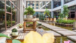 Un edificio moderno con grandes ventanales, una fuente central y plantas en macetas.