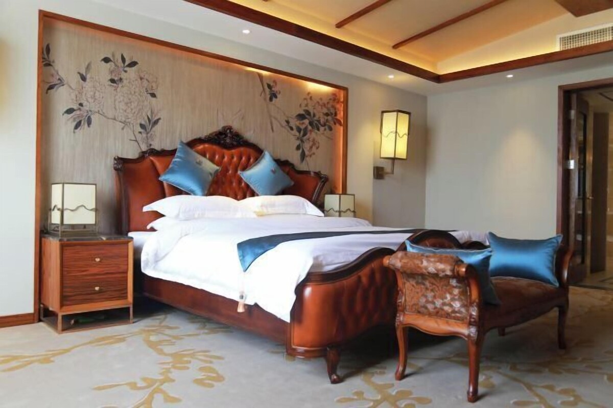 Un dormitorio con una cama grande, cabecera de madera, dos mesitas de noche, una silla y una lámpara de pared.
