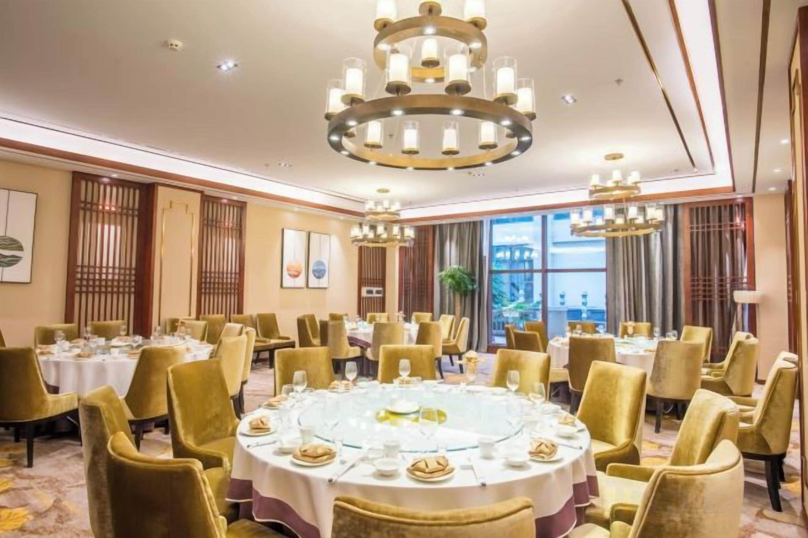 A hotel dining room with round tables, gold chairs, and chandeliers.