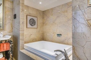 Un baño con pared de mármol, una obra de arte enmarcada y una bañera blanca.
