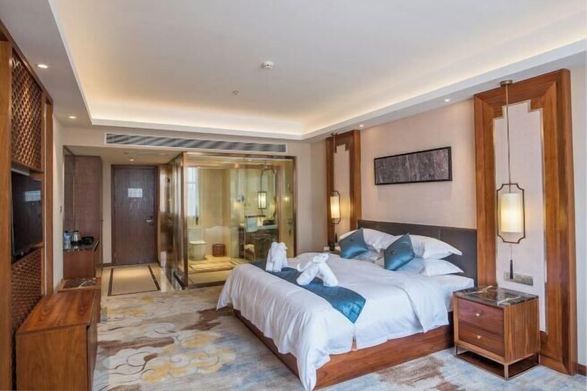 Habitación de hotel con una cama grande, una mesita de noche de madera, un espejo y un televisor.