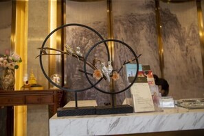 A reception desk with a metal sculpture of branches and birds, a vase with flowers, and a menu stand. - Yuanmou Grand Hotel (Yuanmou)