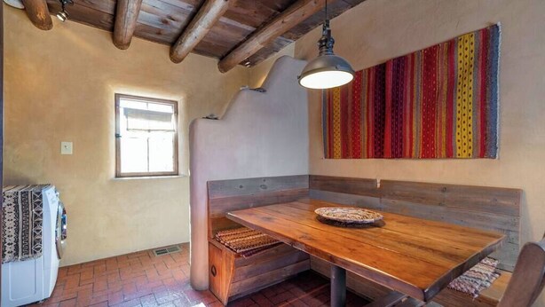 A rustic room with a wooden bench, a table, a hanging light fixture, and a window. - Canyon Getaway- Courtyard -Canyon Rd & Plaza -1BR (Santa Fe)