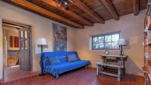 A room with a blue sofa, a wooden table, a lamp, a window, and a stone wall. - Canyon Getaway- Courtyard -Canyon Rd & Plaza -1BR (Santa Fe)