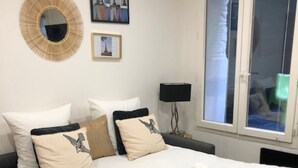 A neatly made bed with white linens, a round wall mirror, and two framed pictures on the wall.