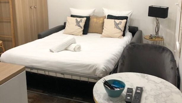A bedroom with a bed, a round mirror, a television, and a small table with a bowl and remote controls.