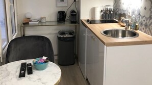 A compact kitchen with a sink, a coffee machine, and a microwave. There is a small table with a bowl and remote controls.