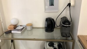 A glass-top table with a coffee maker, a kettle, a book, a decorative item, and a framed picture on the wall.