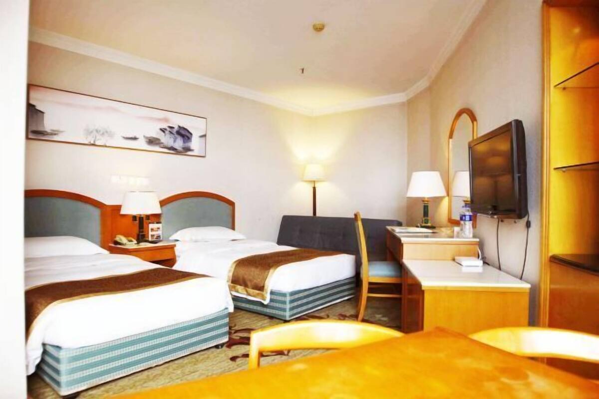 A hotel room with two beds, a desk, a chair, a television, and a painting on the wall.