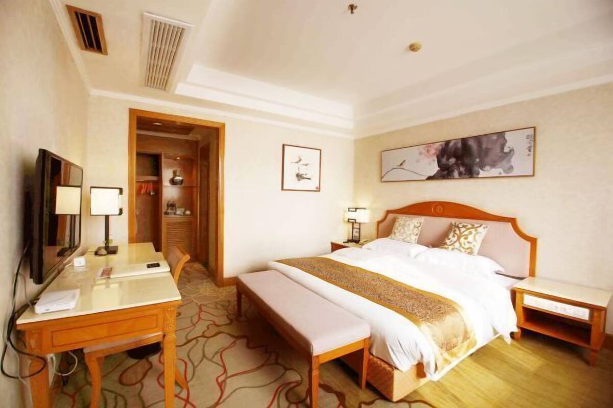 A hotel room with a bed, bedside tables, a desk, a chair, and a television.