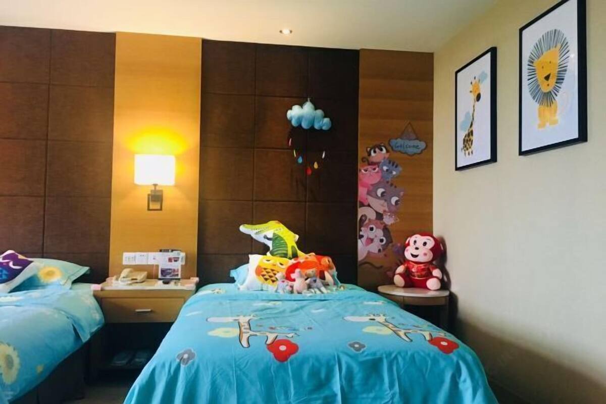 A hotel room with two beds, a nightstand, a lamp, and wall decorations including framed pictures and a cloud-shaped decoration.