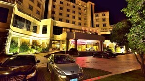 Ein Hotel mit mehreren Etagen, einem gut beleuchteten Eingang und einigen parkenden Autos.