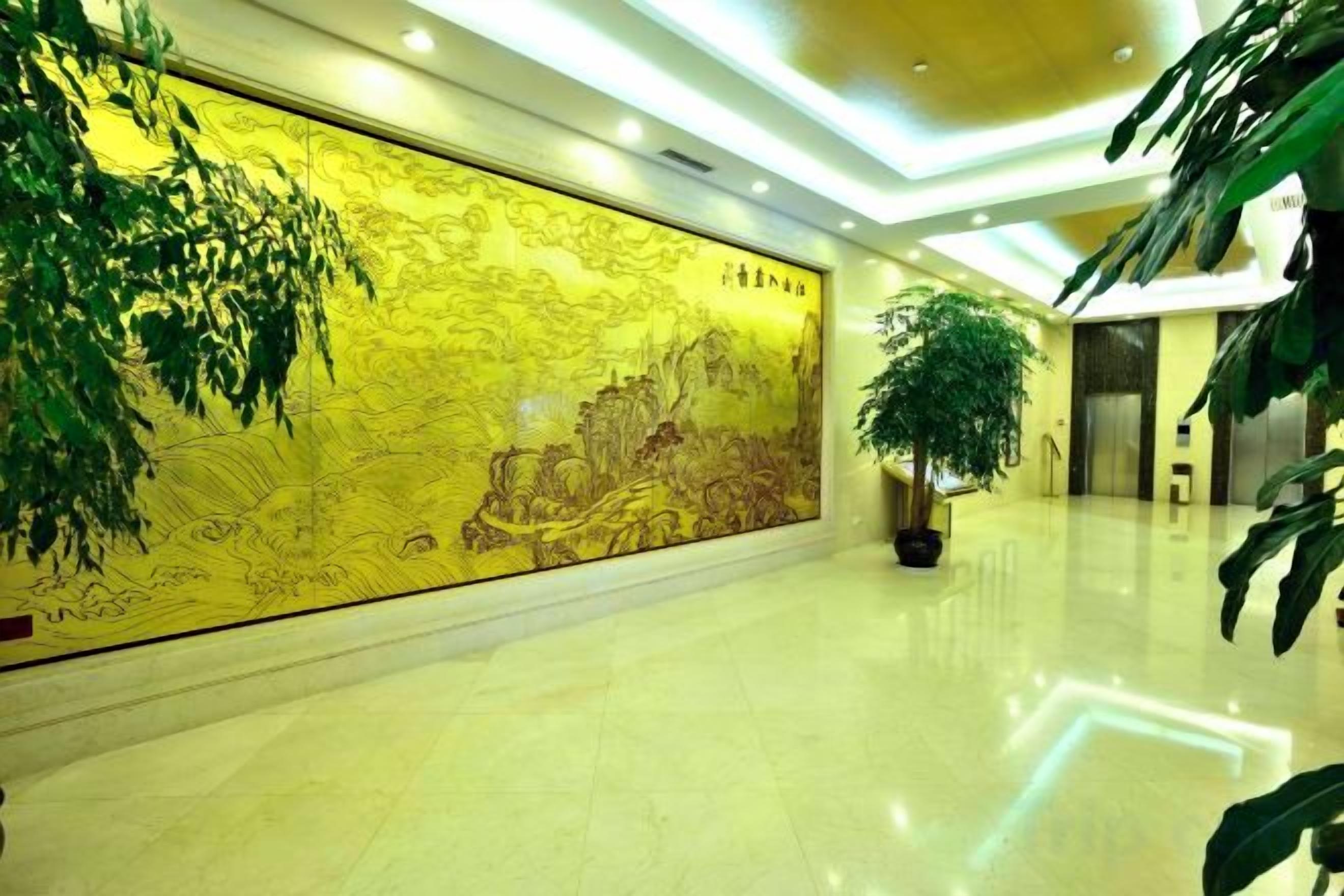 A spacious lobby with a large golden mural, a polished floor, and potted plants.